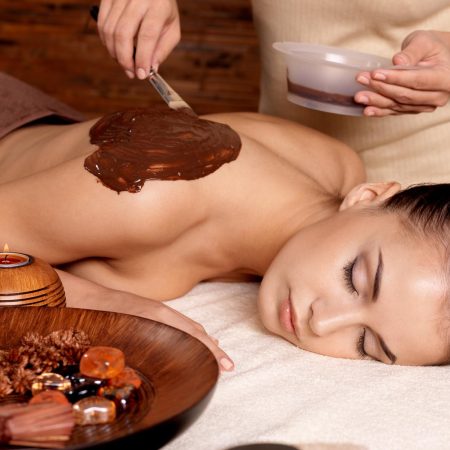 Spa therapy for young woman receiving cosmetic mask on back at beauty salon